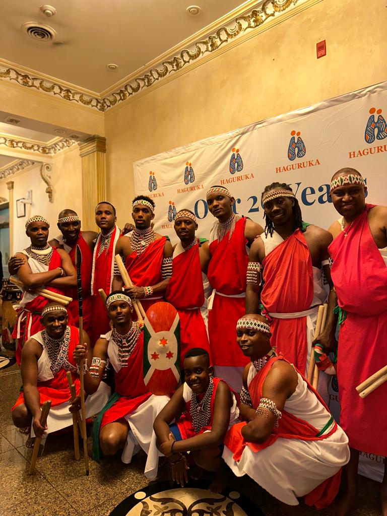 The full Remesha Drums ensemble posed together in red and white regalia with the Burundian flag shield