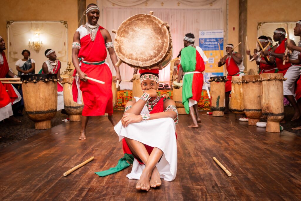 A drummer balancing an Ingoma drum on his head while the ensemble plays behind him